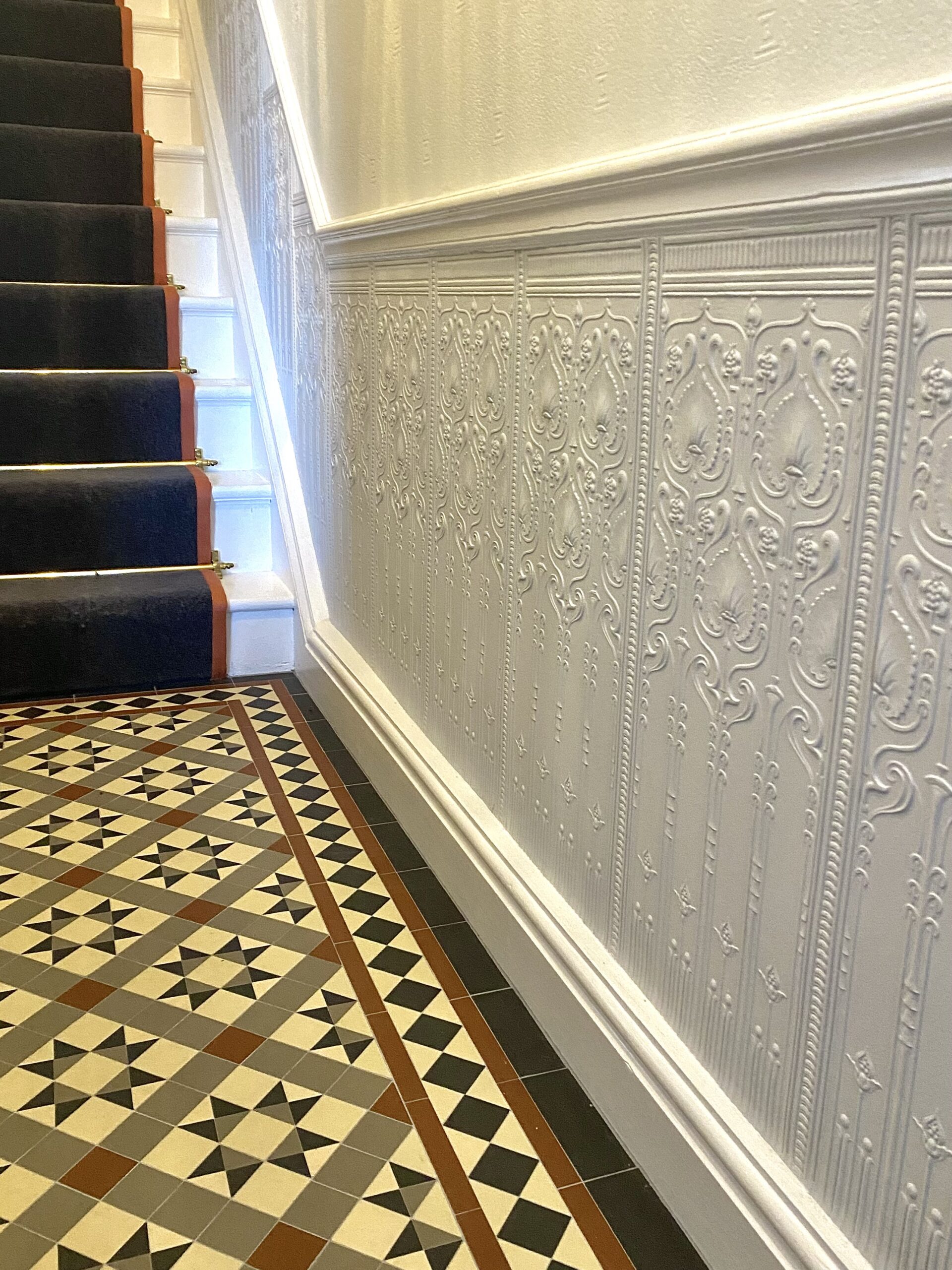 Hallway image with Lincrusta dado panelling, victorian floor tiles and stair grey stair carpet held in place by brass stair rods.